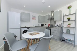A modern kitchen with a white refrigerator, grey cabinets, a round dining table with four chairs, and a built-in oven.