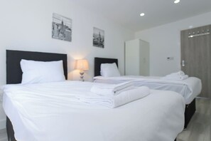A hotel room with two beds, a nightstand with a lamp, and a wardrobe.