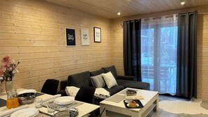 Een gezellige woonkamer met een houten wand, een zwarte bank, een eettafel gedekt met borden, glazen en een bloemenvaas.