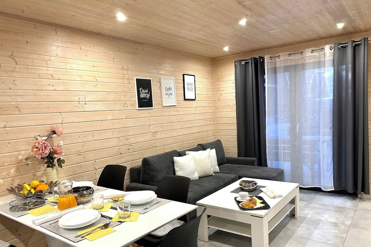 Una sala moderna con comedor, paredes de madera, un sofá gris y una mesa de comedor para dos.