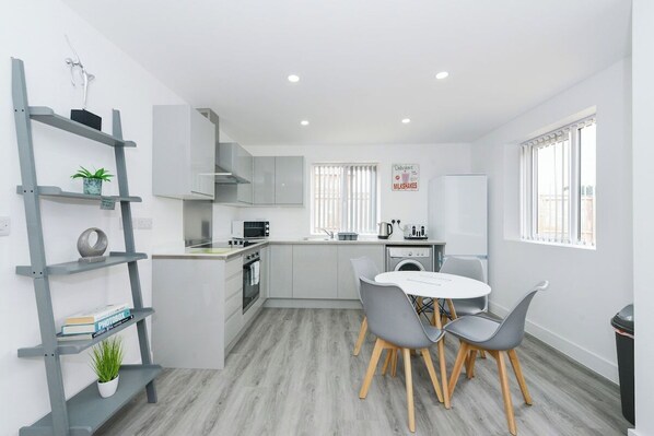 A modern kitchen with a dining area, white cabinetry, and a grey shelving unit. - 2-BR Flat w/ Free Parking Near Nottingham (Gedling)