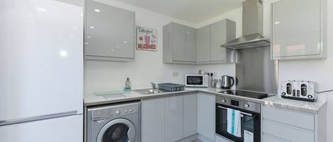A modern kitchen with a washing machine, microwave, oven, and a toaster.