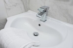 A white bathroom sink with a chrome faucet, a towel, and a marble wall. - Apartment w/ Parking Close to Nottingham (Gedling)