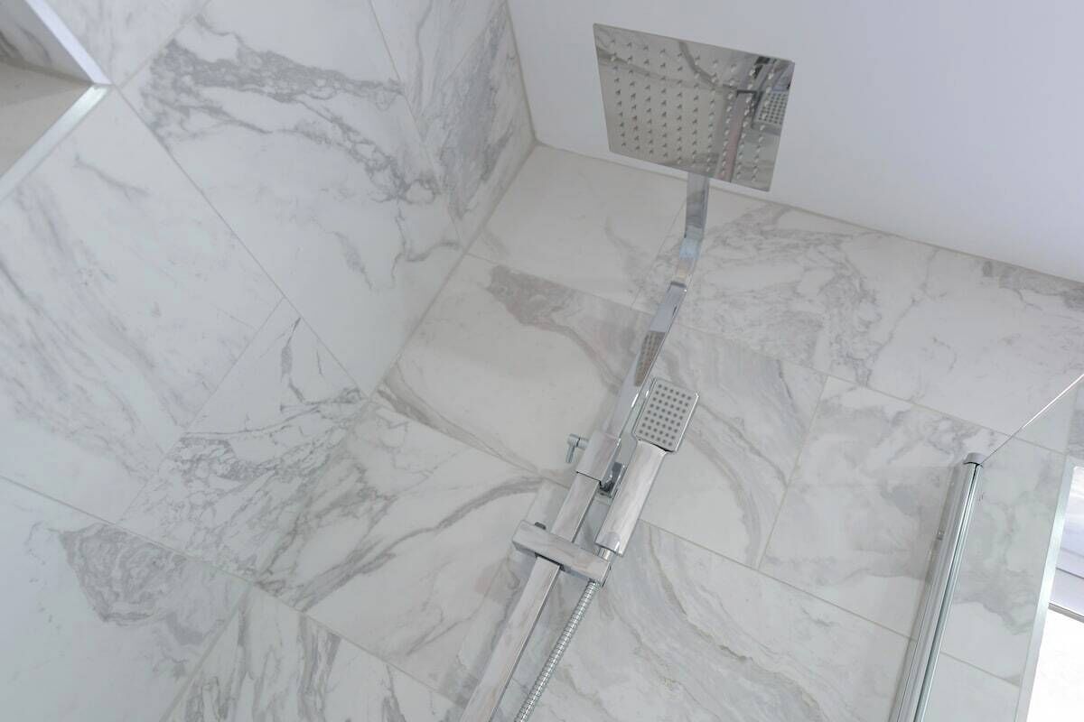 A shower with a handheld showerhead and a wall-mounted control panel.