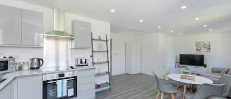 A modern kitchen with built-in appliances, a dining area with a table and chairs, and a living space with a sofa and TV.