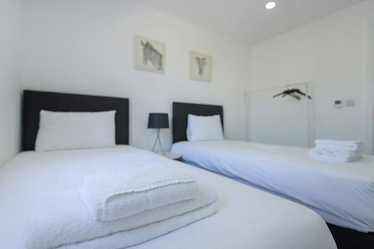 A hotel room with two beds, white linens, and a mirror with a towel rack.