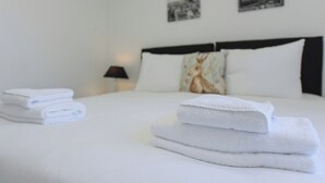 A neatly made bed with folded white towels, a black headboard, and two black-and-white cityscape pictures on the wall. - 2-BR Stay w/ Parking Near Nottingham (Carlton)
