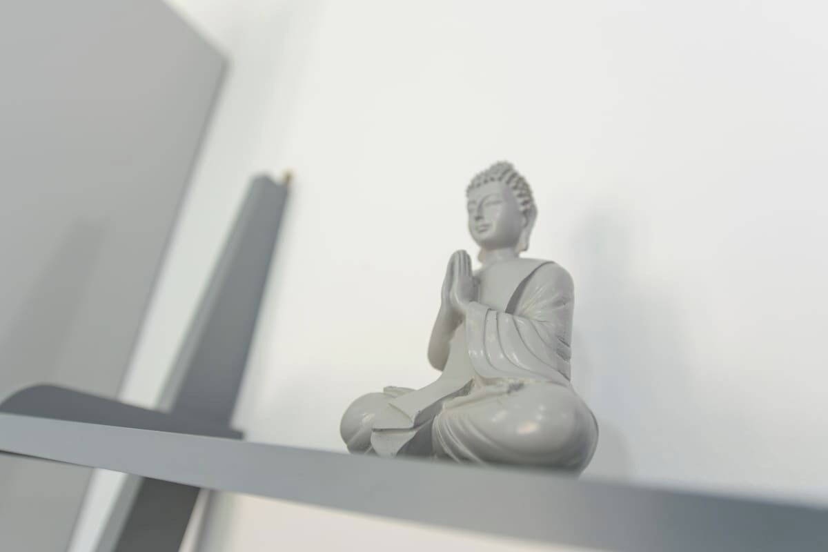 Eine weiße Statue einer sitzenden Figur auf einem Regal.