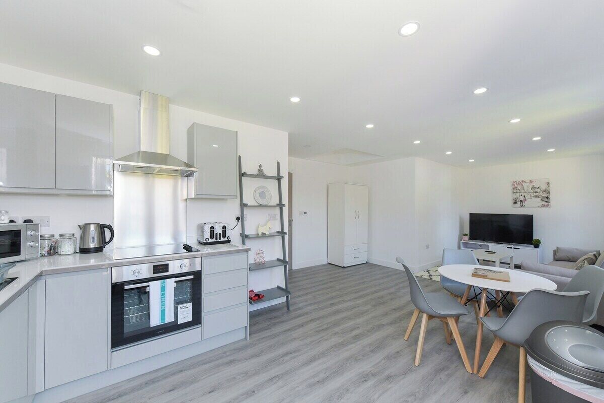 A modern kitchen with built-in appliances, a dining area with a table and chairs, and a living space with a sofa and TV.