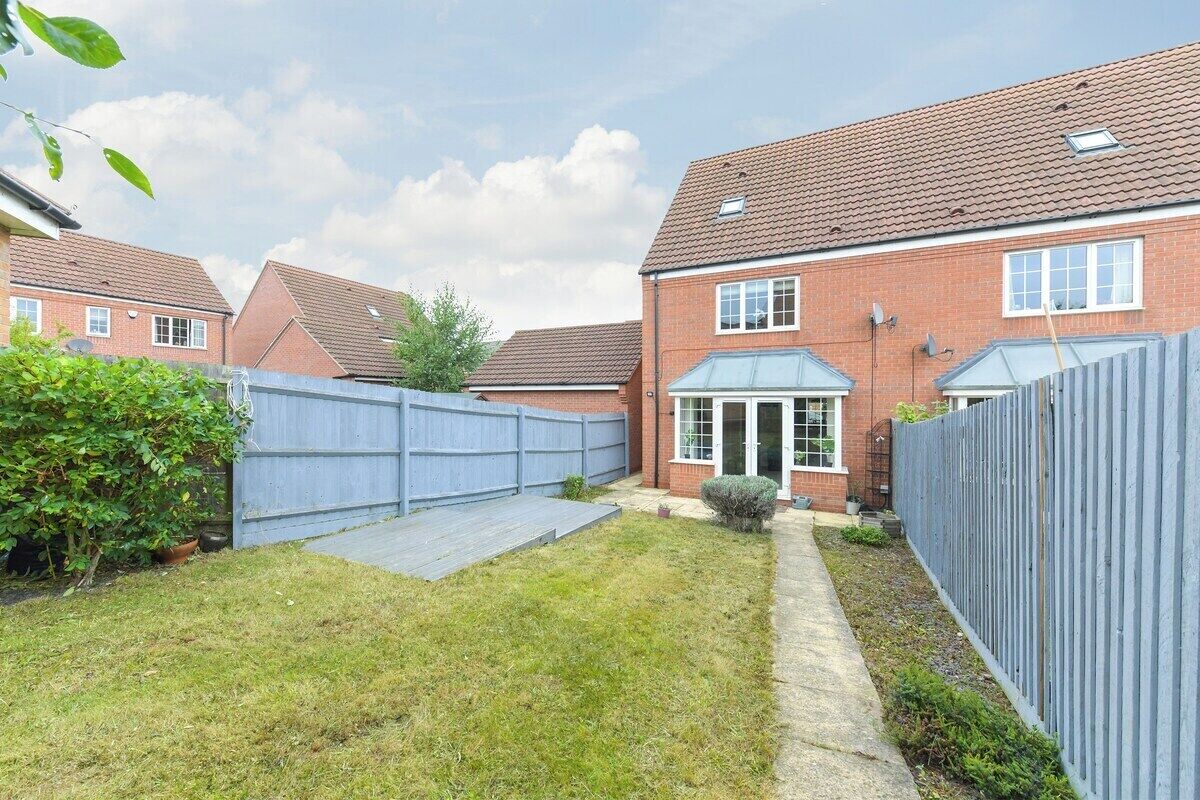 A residential property with a paved driveway, a fenced backyard, and a brick house with a tiled roof.