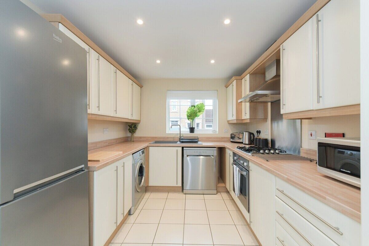 A modern kitchen with a stainless steel refrigerator, built-in dishwasher, microwave, and stove. There is a window with a view of buildings outside.