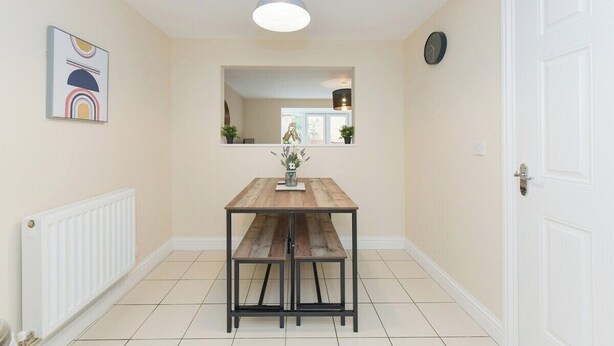Un pasillo con una mesa tipo banco de madera, un radiador, un reloj y una puerta.