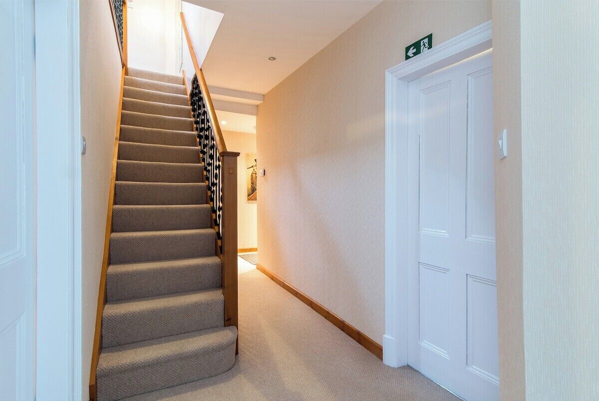 A carpeted staircase with a handrail, a white door, and a wall-mounted exit sign.