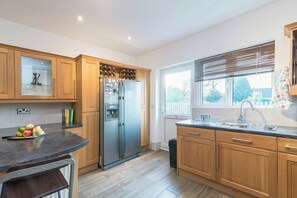 Une cuisine moderne avec des meubles en bois, un réfrigérateur en acier inoxydable, un plan de travail noir et une fenêtre équipée de stores.