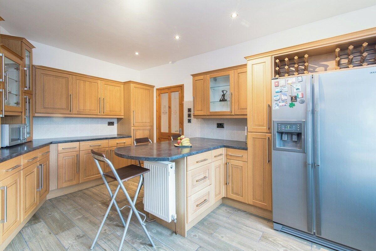 Eine Küche mit Holzschränken, einem Edelstahlkühlschrank und einem Barhocker.