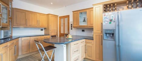 A kitchen with wooden cabinets, a stainless steel refrigerator, and a bar stool.