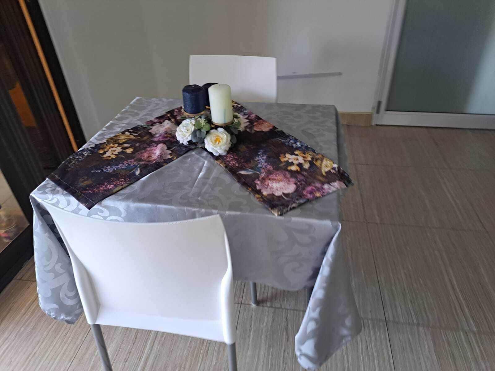 A dining table with a floral tablecloth, a white chair, and a candle centerpiece.