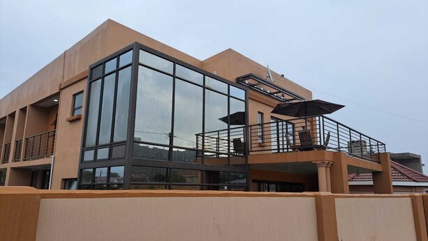A modern two-story building with large glass windows and a balcony with outdoor furniture. - Jate Guest House (Maseru)