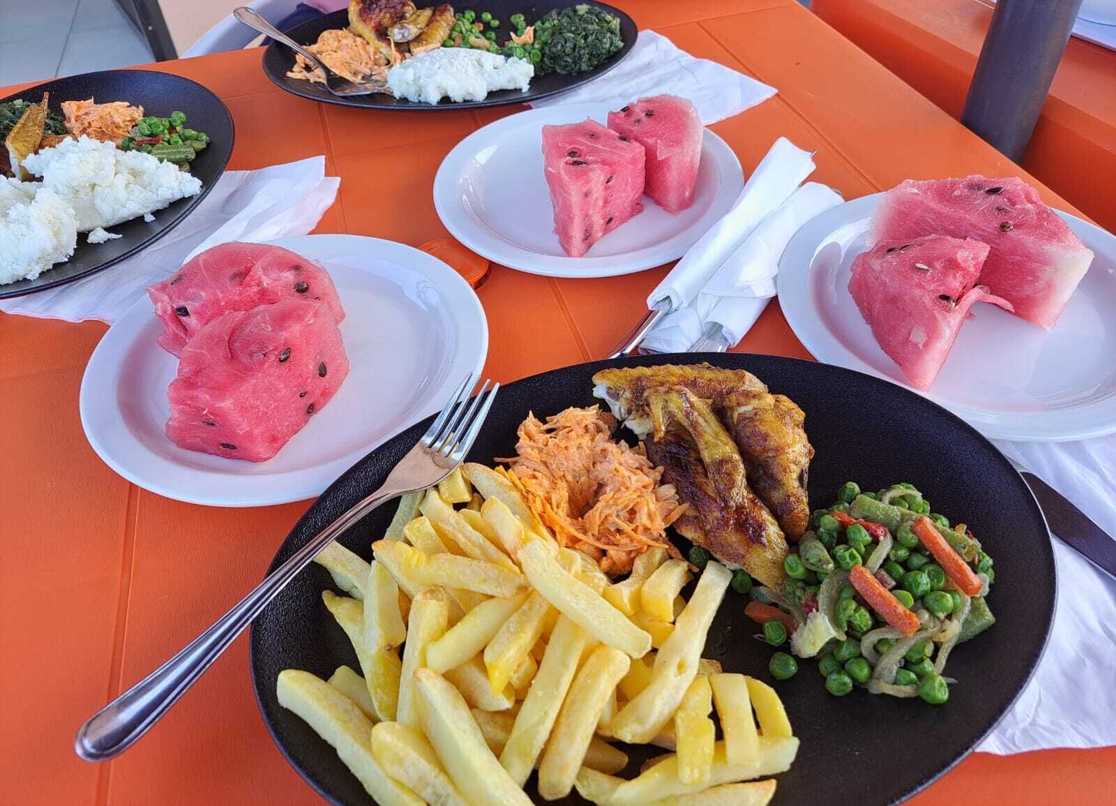 Een tafel met diverse gerechten, waaronder rijst, watermeloen, friet en een visgerecht.