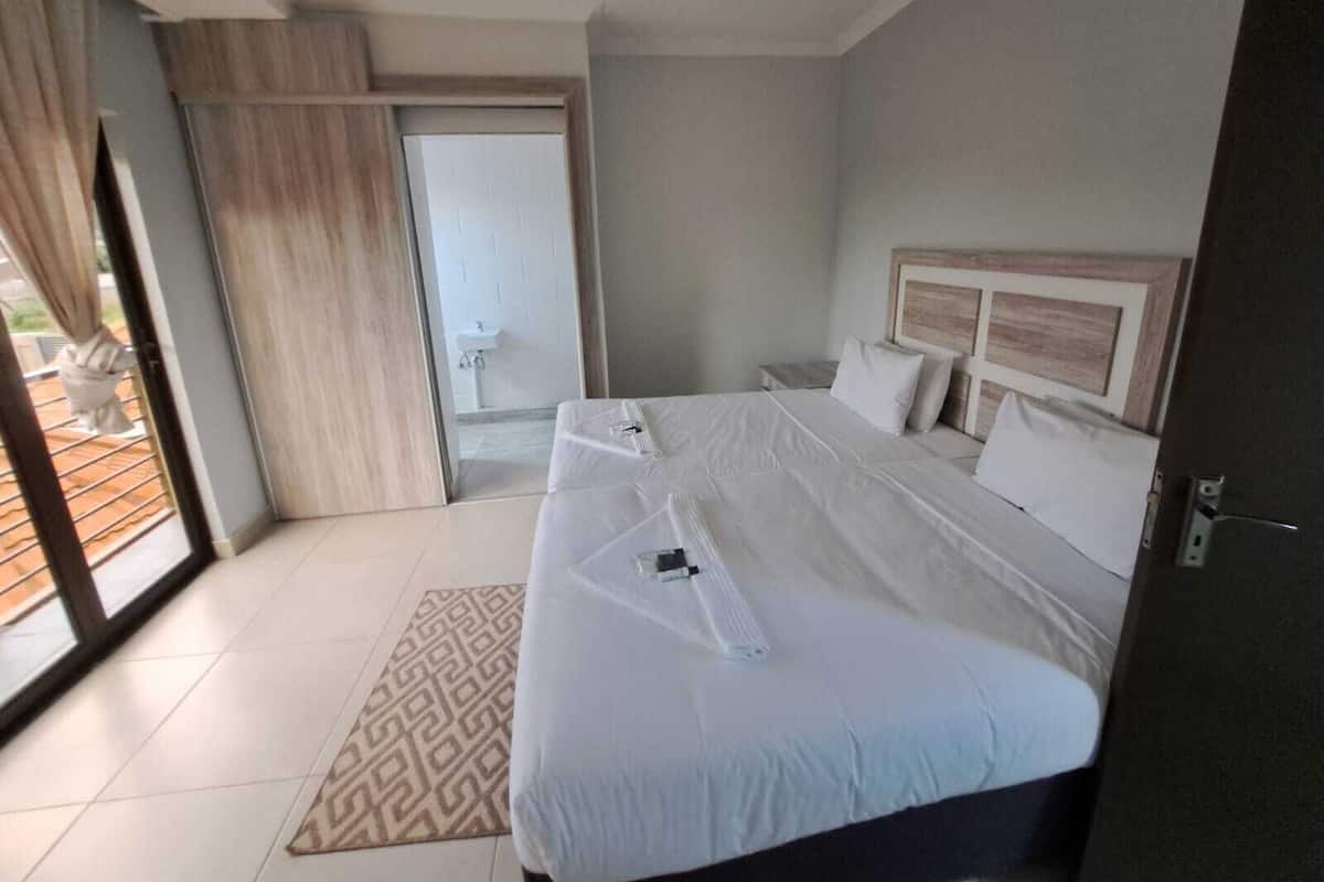 A hotel room with a large bed, a bedside table, a nightstand, and a view through a sliding door to an outdoor area.
