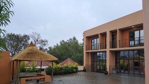 A courtyard with a thatched-roof structure, a building with balconies, and a paved ground. - Jate Guest House (Maseru)