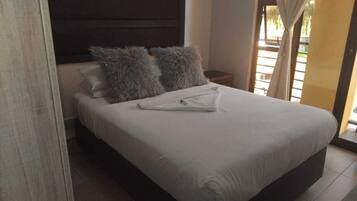 A bed with a white mattress and two grey pillows, a wooden headboard, and a nightstand with a lamp.