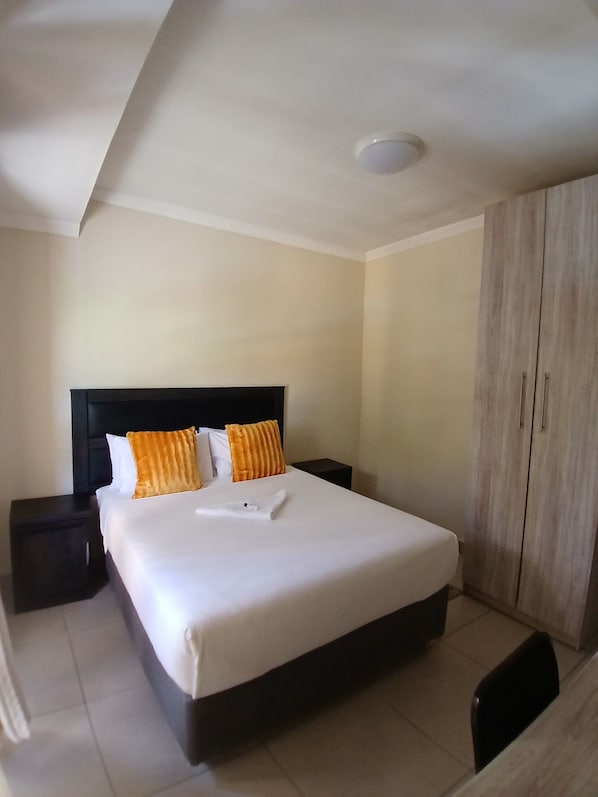 Una habitación de hotel con una cama grande, una mesita de noche, un armario y una lámpara de techo.