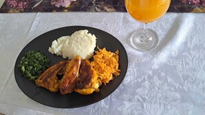 A plate of food with rice, greens, and meat, and a glass of orange juice on a table with a floral tablecloth. - Jate Guest House (Maseru)