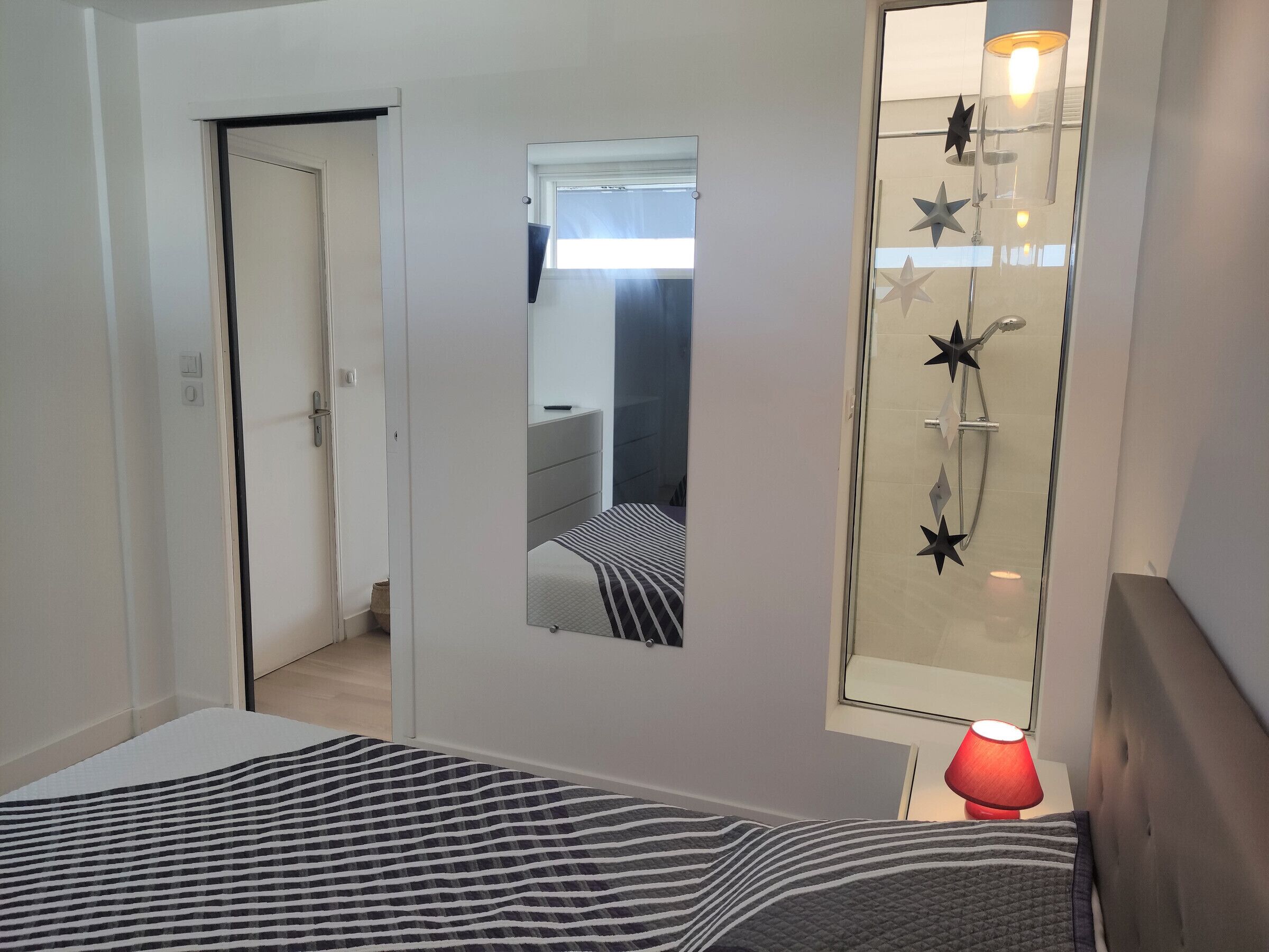 A bedroom with a bed, a bedside table with a lamp, a mirror, and a shower with star-shaped showerheads.