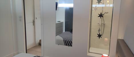 A bedroom with a bed, a bedside table with a lamp, a mirror, and a shower with star-shaped showerheads.