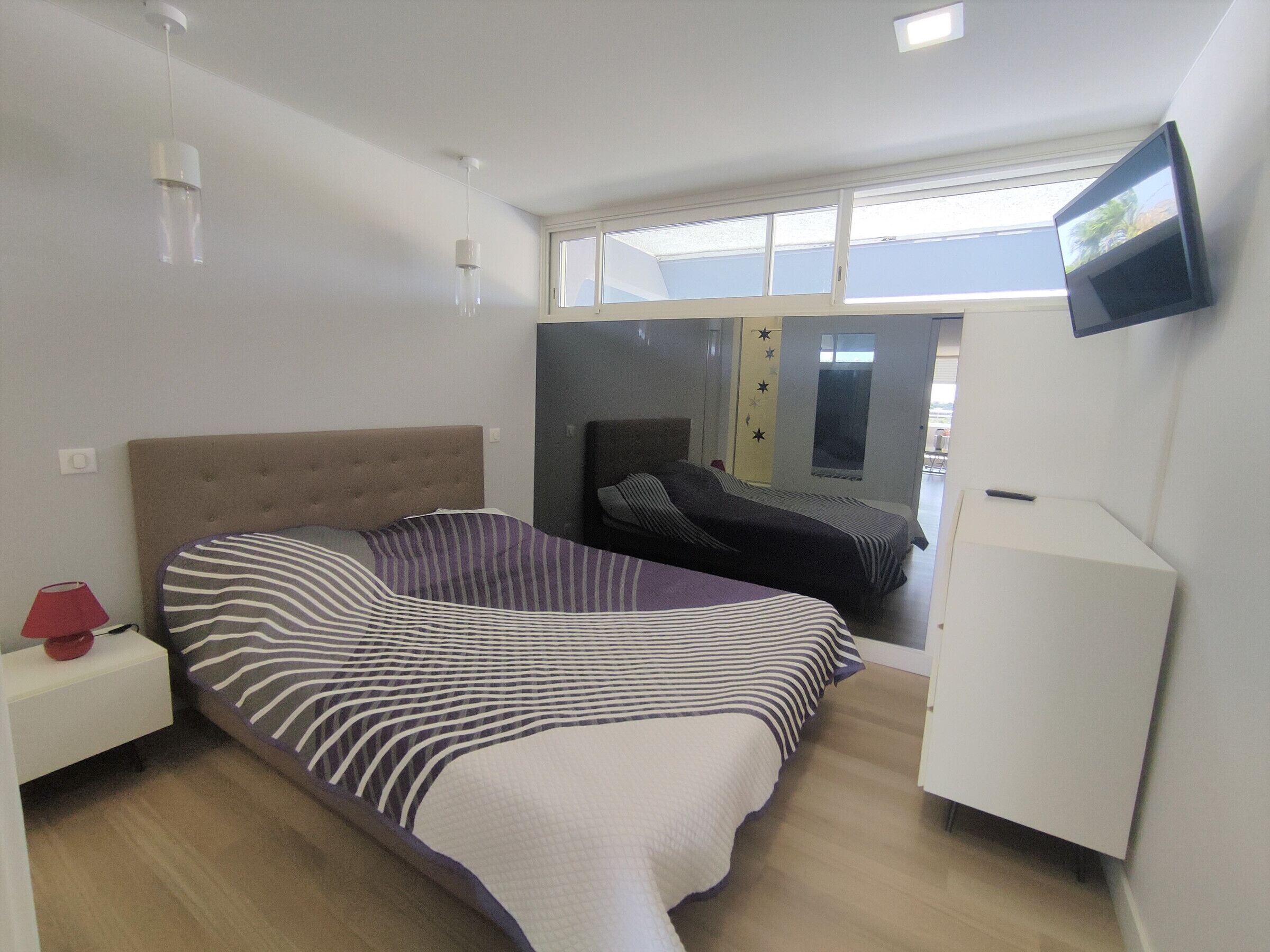 A bedroom with a bed, bedside table, lamp, TV, and a window.