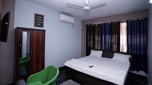 Un dormitorio con cama, ventilador de techo, aire acondicionado, una silla verde y un armario de madera.