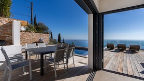 Een houten terras met een tafel en stoelen, uitkijkend op een helderblauwe lucht en een wateroppervlak.