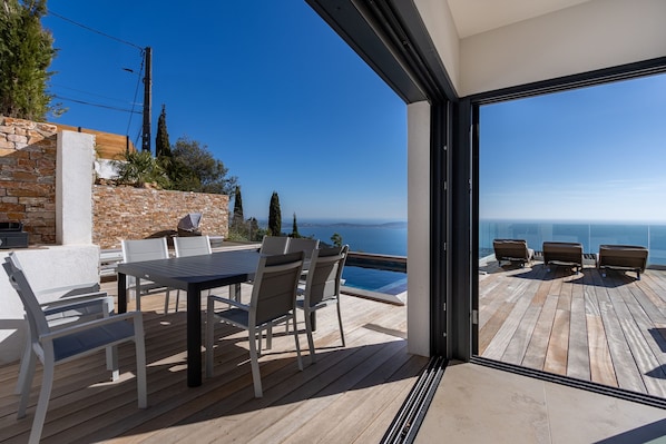 Une terrasse en bois avec une table et des chaises, d’où l’on peut admirer un ciel bleu dégagé et une étendue d’eau.