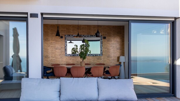 Een moderne woonkamer met een bank, een eethoek met tafel en stoelen, en een groot raam met uitzicht.