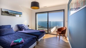 Een moderne slaapkamer met twee bedden, een grote schuifpui naar een balkon en uitzicht op zee.
