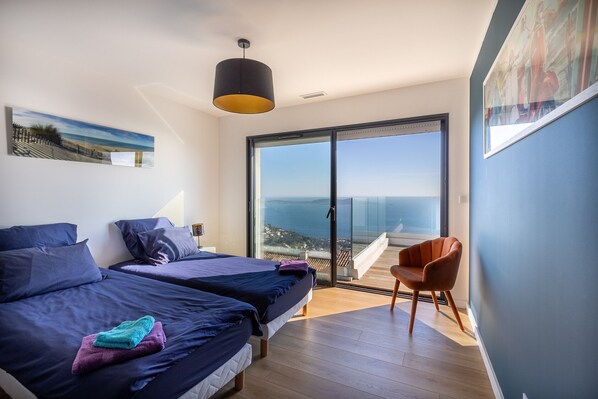 A modern bedroom with two beds, a large sliding glass door to a balcony, and a view of the sea. - Breathtaking Sea View Villa - Prestige and Calm (Carqueiranne)