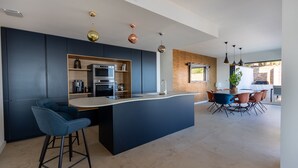 Een moderne keuken met donkere kastjes, een centraal eiland en een eetgedeelte met een accentmuur van baksteen.