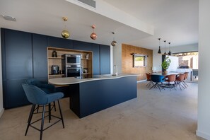 Eine moderne Küche mit dunklen Schränken, einer zentralen Kochinsel und einem Essbereich mit einer Wand aus Ziegelsteinen.