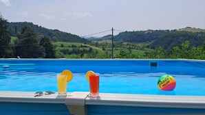 A swimming pool with three glasses of drinks and a beach volleyball on the edge. - Family apartment: sleeps 6, Use of garden, sunbeds and swimming pool. (Monte San Pietro)