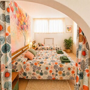 A cozy bedroom with a bed, a bedside table, a lamp, a window with curtains, a radiator, and a potted plant. - Family apartment: sleeps 6, with a garden, lounge chairs, and a pool (Monte San Pietro)