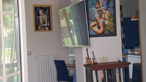 A living room with a large TV, a bookshelf, and two paintings on the wall. - Family apartment: sleeps 6, Use of garden, sunbeds and swimming pool. (Monte San Pietro)