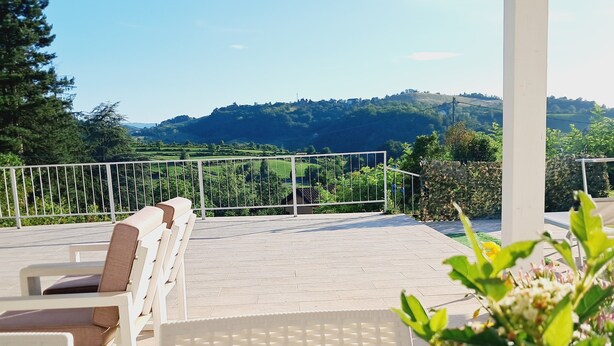 A terrace with white chairs and a table, overlooking a scenic landscape with hills and trees. - Family apartment: sleeps 6, Use of garden, sunbeds and swimming pool. (Monte San Pietro)