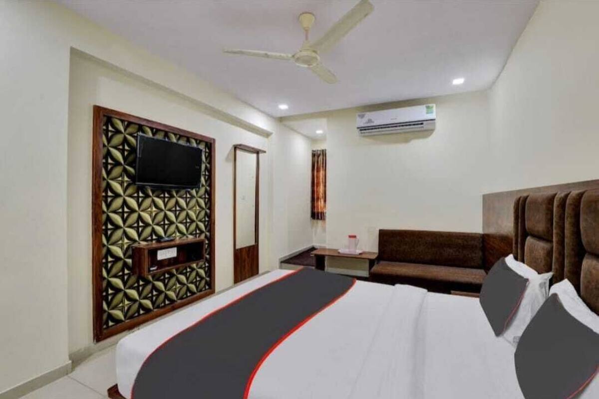 Quarto de hotel com cama, televisão presa a um painel decorativo, ventoinha de teto e ar condicionado.