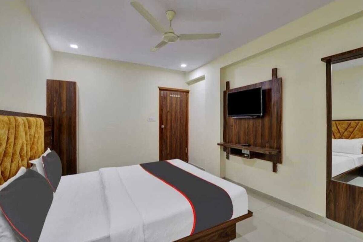 Quarto de hotel com cama, ventoinha no teto, televisão fixada na parede e guarda-roupa de madeira.