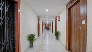 A long, narrow hallway with a tiled floor, two potted plants, and wooden doors on either side. - Hotel Neelkamal (Ahmedabad)
