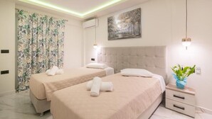 Quarto de hotel com duas camas, uma janela grande com cortinas, um quadro na parede e uma mesa de cabeceira com uma planta.