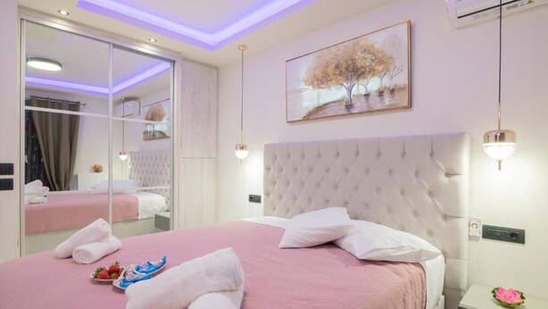Quarto de hotel com uma cama grande, um espelho, um quadro e uma mesa de cabeceira com uma flor.