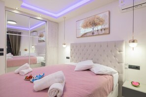 Una habitación de hotel con una cama grande, un espejo, un cuadro y una mesita de noche con una flor.