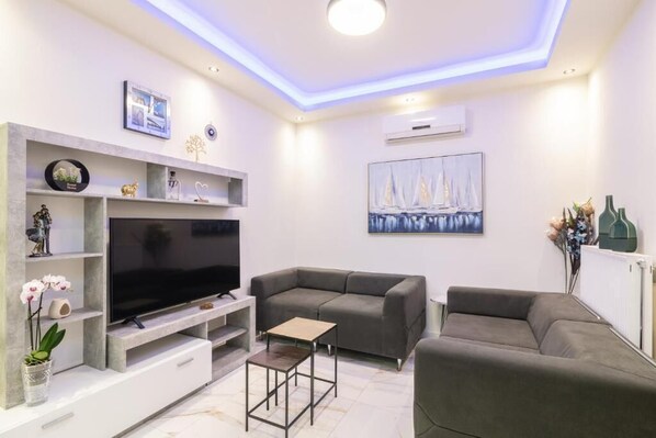 Una sala de estar moderna con un televisor de pantalla plana, sofás grises, una mesa de centro y objetos decorativos en estantes.